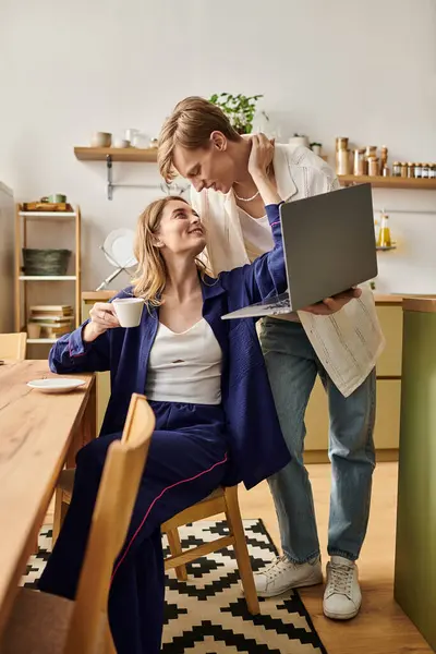 Young couple shares a loving moment at home, enjoying coffee and working together on a laptop. — Stock Photo
