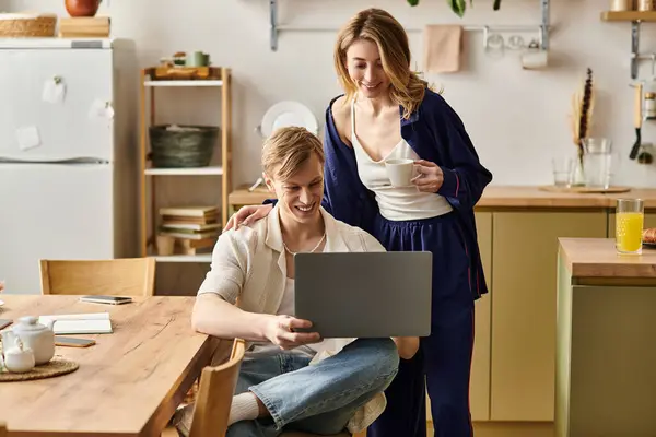 A loving couple relaxes in their stylish kitchen, sharing smiles over a laptop and warm drinks. — Stock Photo