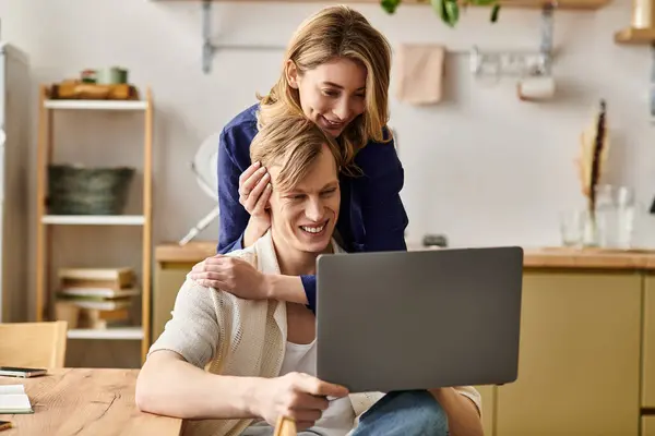 In a cozy home, a young couple sits together, sharing joyful moments while looking at a laptop. — Stock Photo