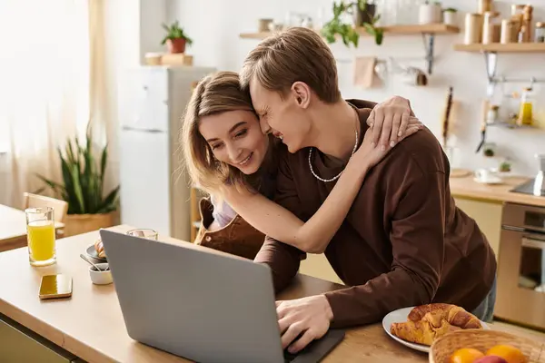 A happy couple smiles and embraces while watching something exciting on their laptop. — Stock Photo