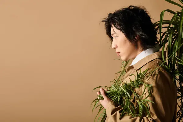 Asiatique homme en tenue de printemps à la mode pose gracieusement avec de la verdure dans un cadre chic studio. — Photo de stock