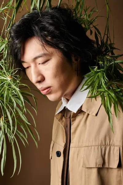 Un hombre asiático de moda presenta estilos de primavera en un entorno de estudio único con exuberante vegetación. - foto de stock