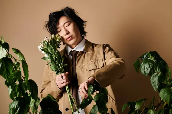 A trendy Asian man poses in a studio, holding flowers while showcasing spring fashion. — Stock Photo