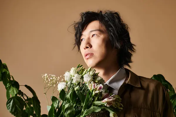An Asian man elegantly poses in a studio with fresh blooms in trendy spring attire. — Stock Photo