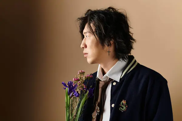 An asian man poses elegantly in a studio, showcasing spring fashion while holding fresh flowers. — Stock Photo