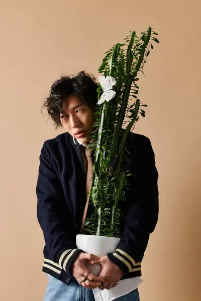 An Asian man in fashionable spring attire poses with a large plant in a studio atmosphere. — Stock Photo