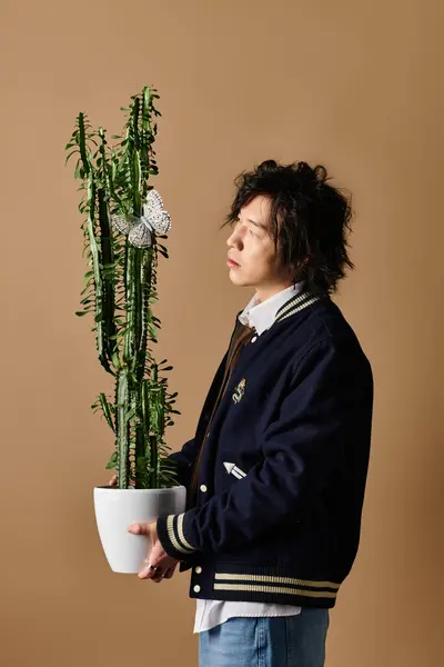 A stylish man in trendy attire poses with a tall cactus in a contemporary studio. — Stock Photo