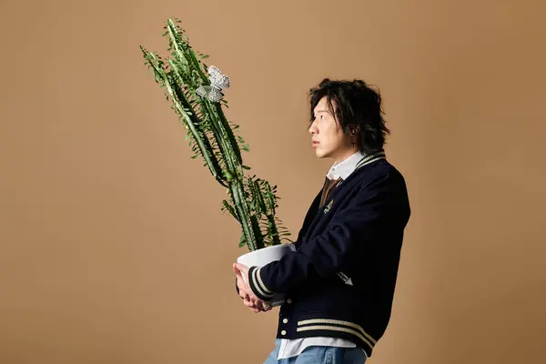 An asian man poses confidently in fashionable attire while holding a pot of lush greenery. — Stock Photo