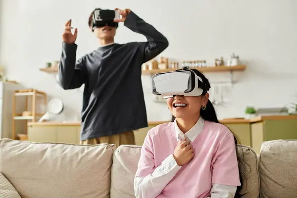 A young asian couple experiences virtual reality in their cozy home, laughing and sharing joy. — Stock Photo