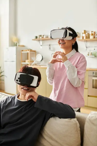 A young couple engages with virtual reality headsets, sharing laughter and excitement at home. — Stock Photo
