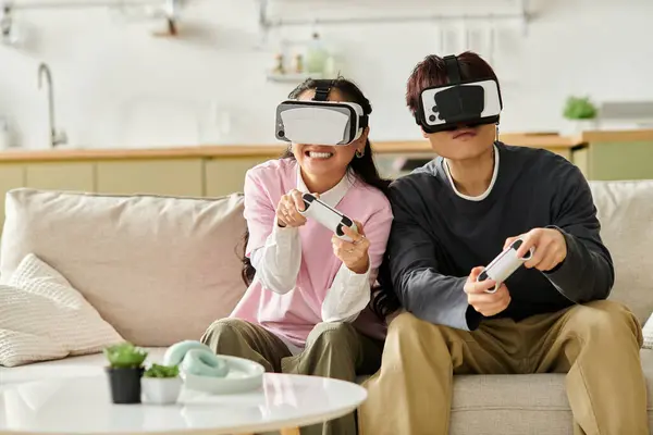 Una joven pareja sonríe mientras se sumerge en una sesión de juego de realidad virtual en casa. - foto de stock
