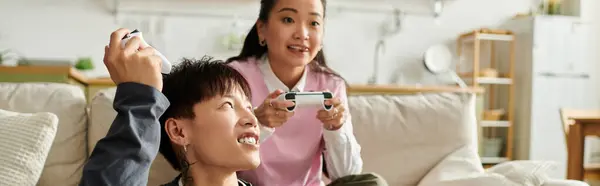 A joyful young asian couple engages in a gaming session at home, immersed in shared excitement, banner — Stock Photo