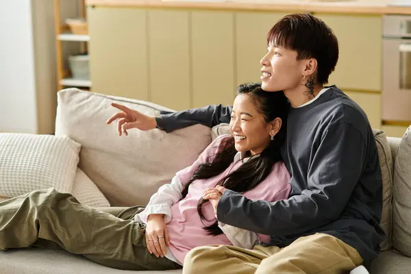 A happy young asian couple relaxes on their cozy couch, sharing joyful moments. — Stock Photo