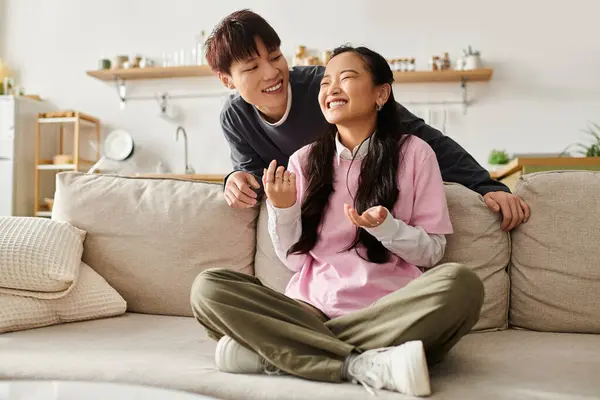 A young Asian couple playfully chats on a cozy couch at home, radiating joy. — Stock Photo