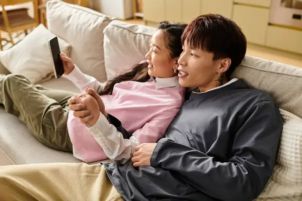 Loving young couple relaxes on their couch, sharing laughter while looking at a mobile device. — Stock Photo