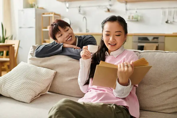 In a warm home setting, a young couple shares a joyful moment as the woman reads and the man smiles. — Stock Photo