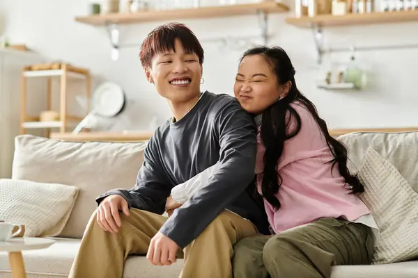 A young asian couple laughs together on a comfortable couch, enjoying quality time at home. — Stock Photo