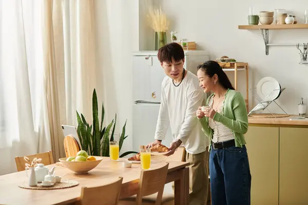 A young couple smiles and enjoys breakfast at home, surrounded by fresh fruit and sunlight. — Stock Photo