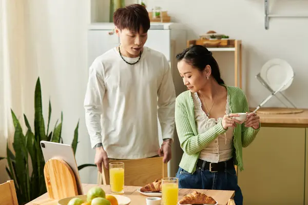 Una giovane coppia asiatica prepara la colazione insieme, godendo di tempo di qualità nella loro casa accogliente. — Foto stock