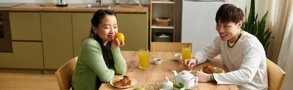 A young couple shares a cheerful breakfast at home, savoring croissants and fresh juice, banner — Stock Photo