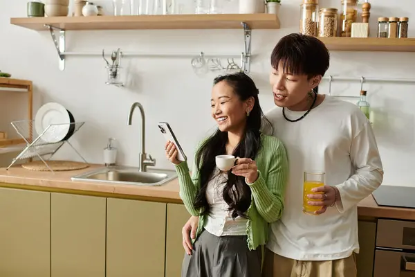 Una joven pareja disfruta del desayuno en casa mientras comparte risas y una pantalla de teléfono. - foto de stock