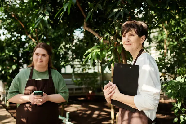 In a lush greenhouse, a woman and her young colleague with Down syndrome share teamwork. — Stock Photo