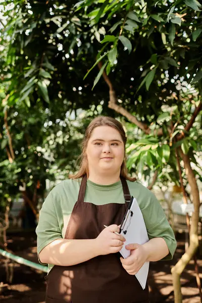Young woman with Down syndrome effectively manages tasks in a flourishing greenhouse setting. — Stock Photo