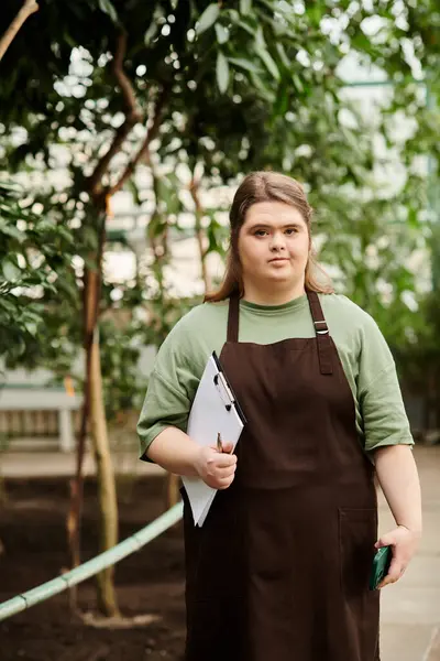 In a lush greenhouse, a confident young woman showcases her dedication to the plants. — Stock Photo