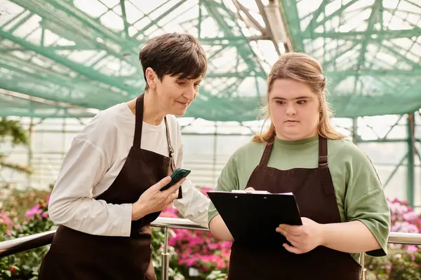 In einem bunten Gewächshaus hilft eine Frau ihrem jungen Kollegen mit Down-Syndrom. — Stockfoto