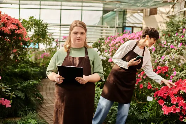 A mature woman and her young colleague work together in a lively greenhouse, tending to flowers. — Stock Photo