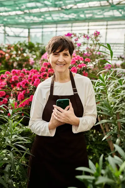 Mature woman exudes confidence while working amidst colorful blooms in a lively greenhouse setting — Stock Photo