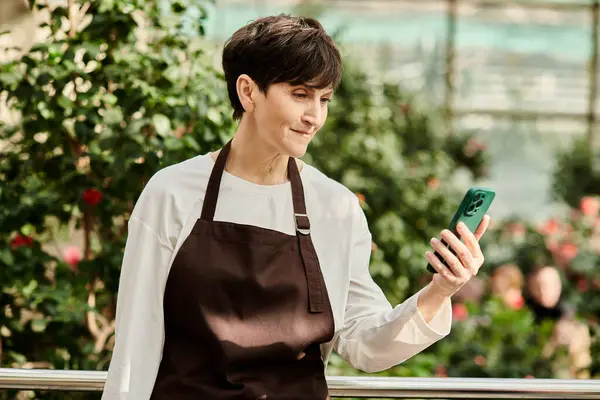 Mature woman in an apron enjoys a moment of connection in a flourishing greenhouse. — Stock Photo