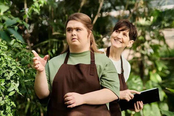 Mature woman engages with a young colleague with Down syndrome while working among lush greenery. — Stock Photo