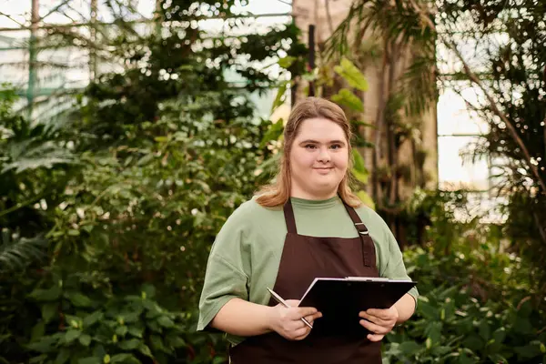 In a vibrant greenhouse, a young woman with Down syndrome shows off her dedication and charm. — Stock Photo