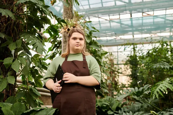 Young woman with Down syndrome shows confidence while working in a lush greenhouse. — Stock Photo