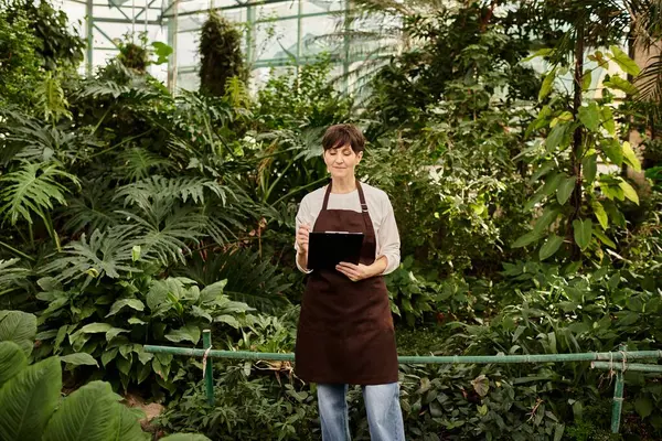 Mature woman confidently manages her tasks in a lush greenhouse environment full of plants — Stock Photo