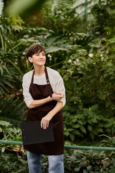Confident woman works diligently in a lush greenhouse, surrounded by vibrant greenery and plants. — Stock Photo
