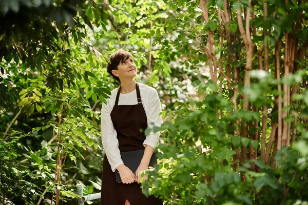 Mature woman confidently works in a thriving greenhouse, surrounded by vibrant plants and greenery. — Stock Photo