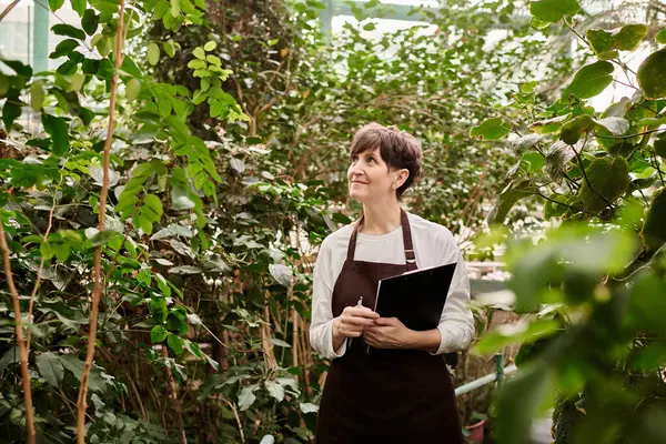 In a vibrant greenhouse, a confident woman examines the plants while working diligently. — Stock Photo