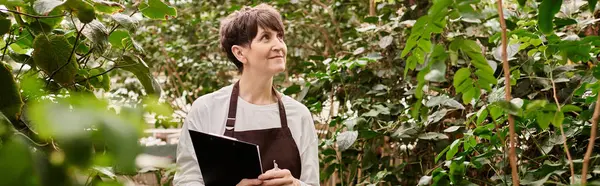 Confident woman enjoying her work amidst lush plants in a lively greenhouse setting. — Stock Photo