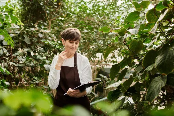Confident woman nurtures plants in a lush, vibrant greenhouse. — Stock Photo