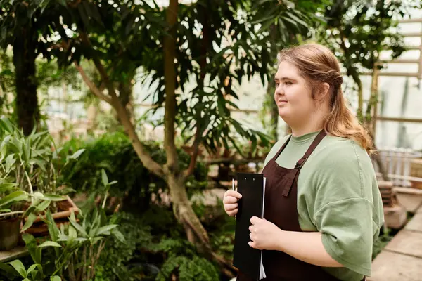 In a sunlit greenhouse, a young woman confidently manages tasks among lush greenery. — Stock Photo