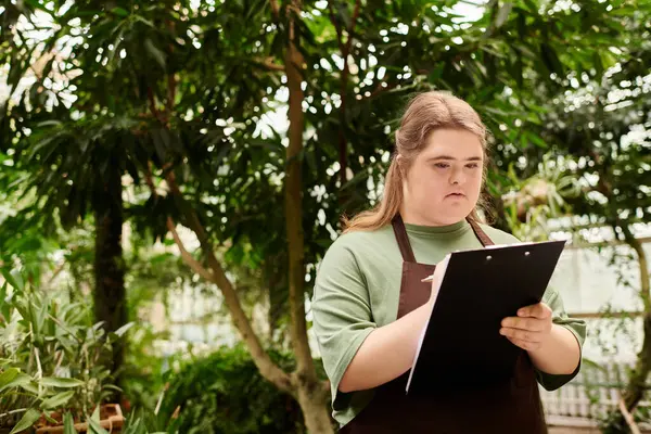 In a lush greenhouse, a young woman with Down syndrome skillfully manages her tasks. — Stock Photo