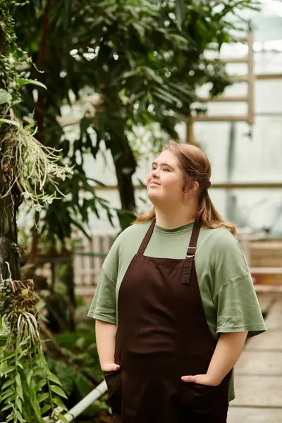 Confident young woman with Down syndrome stands in a lush greenhouse, surrounded by greenery. — Stock Photo