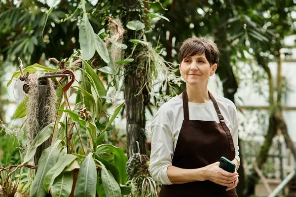 Mature woman showcases her expertise in a vibrant greenhouse, surrounded by flourishing greenery. — Stock Photo