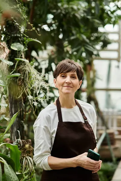 A mature woman embraces her work in a greenhouse, radiating confidence and joy amidst the plants. — Stock Photo