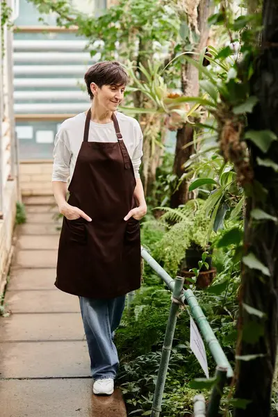 Confident woman joyfully caring for lush plants in a welcoming greenhouse environment. — Stock Photo