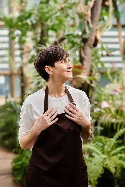 Confident woman enjoys her work in a flourishing greenhouse surrounded by greenery and plants. — Stock Photo