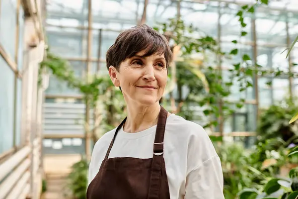 Confident woman in a greenhouse, surrounded by lush greenery, takes pride in her nurturing work. — Stock Photo