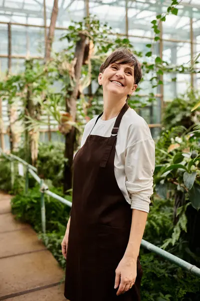 A confident woman in a greenhouse happily cares for vibrant plants amidst stunning greenery. — Stock Photo